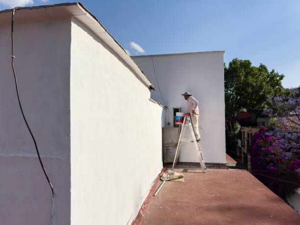 A man painting a white wall, representing the work of exterior painting contractors.