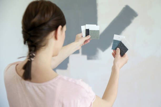 An individual is applying blue paint to a wall with a roller in a home office, highlighting a vibrant color update.