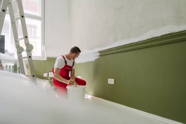 A man is painting a room with green paint, showcasing interior painting services in progress.