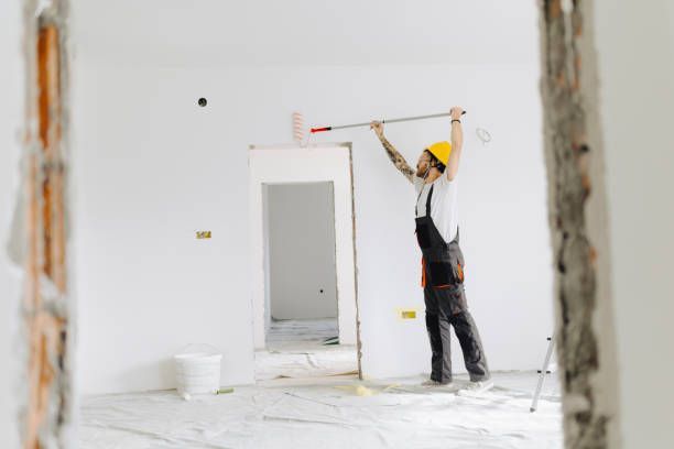 A man in a hard hat holds a paint roller, ready to start interior painting services.