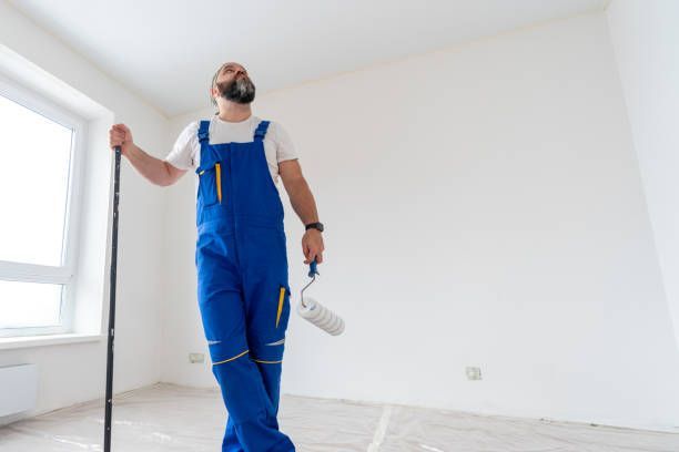 A skilled painter using a ladder is painting a wall, carefully applying paint with a roller to achieve an even and professional finish