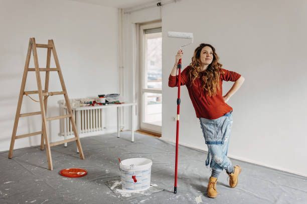 A woman painting a room with a roller, focused on applying a fresh coat of paint to the wall.