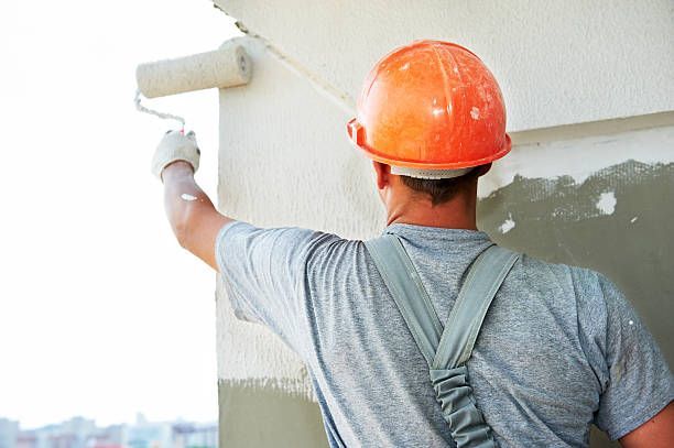 A man wearing an orange hard hat paints a wall, representing Cipriano Painting's work in progress.