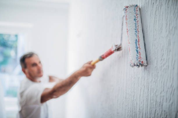 Residential painter applying a fresh coat of paint to a wall with a brush, focusing on even and clean color application.
