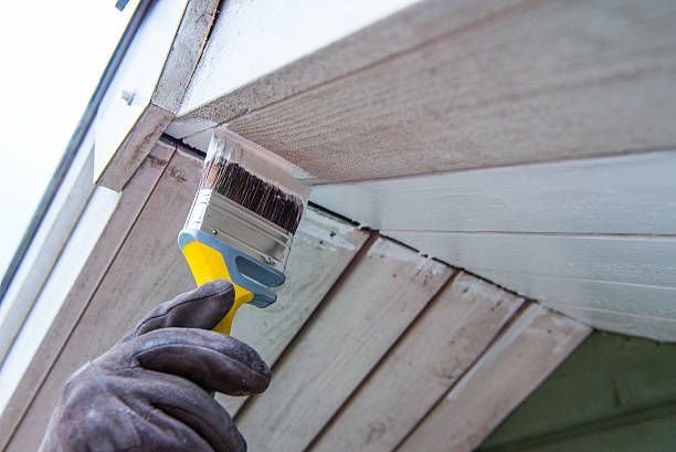 Residential painter using a paintbrush to apply paint to a wall, showcasing detailed home improvement work.