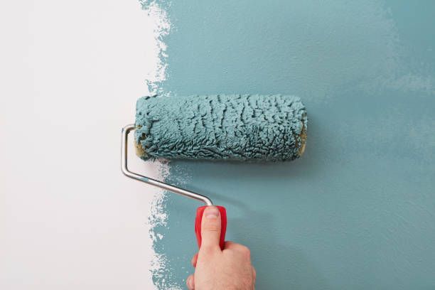 An individual applying exterior paint inside, using a roller to coat the wall with vibrant color, showcasing focus and precision.