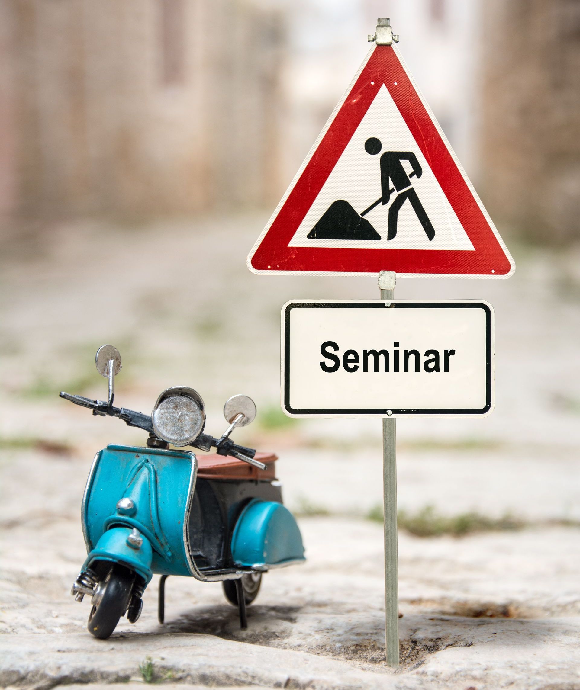 Ein blauer Roller, daneben ein Baustellenschild mit dem Untertitel „Seminar“ Ein blauer Roller, daneben ein Baustellenschild mit dem Untertitel „Seminar“