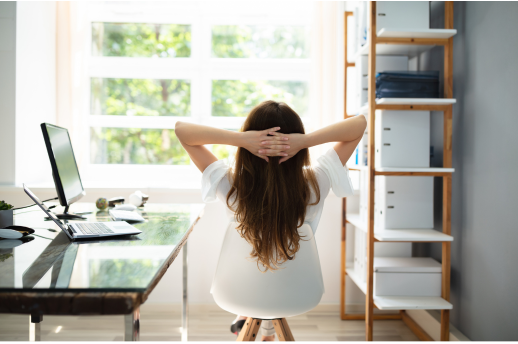 Frau neben Schreibtisch schaut entspannt aus Fenster