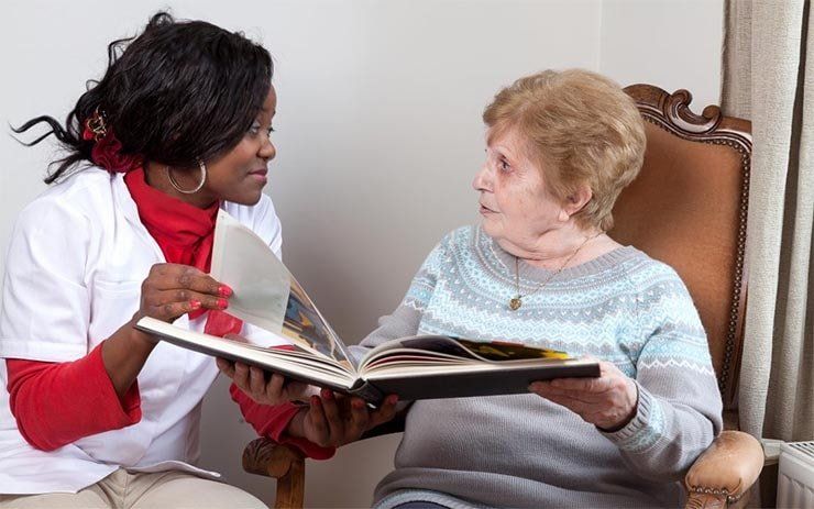 aide à domicile et femme agée discutant en parcourant un album photo