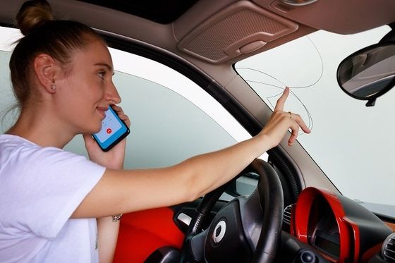 Sostituzione vetri e parabrezza auto La ragazza indica con il dito sul parabrezza rotto, nel frattempo sta chiamando vetri automotive per fare un preventivo di sostituzione parabrezza