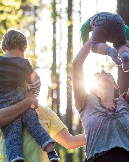 bonheur-famille-lumière-soleil-forêt-bonheur-rire-sourire-tronc-clarté-clairière-arbre-porter-dos-enfant-bras-joie philothérapie-philotherapie-bonheur-famille