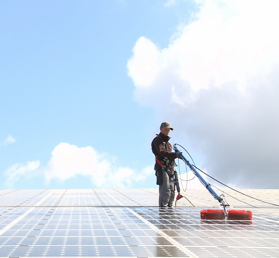 Ein Mann reinigt PV Module auf einem Dach mit einer Reinigungsbürste