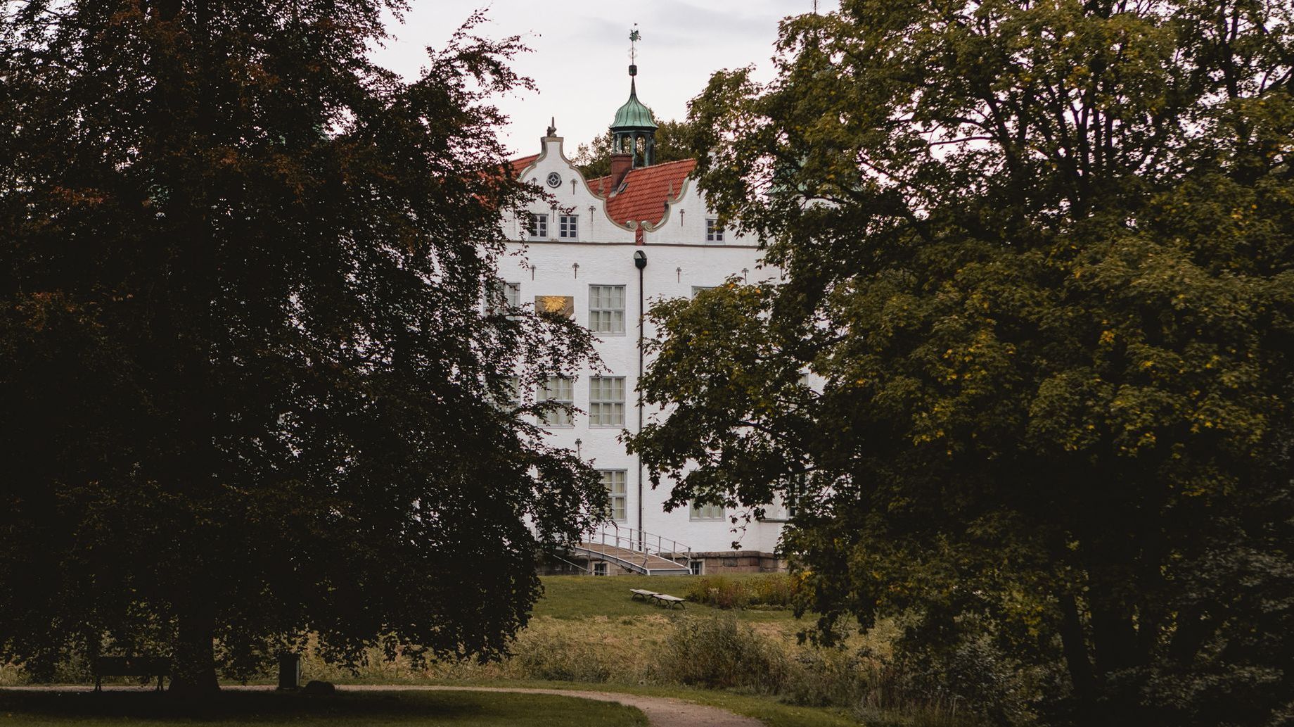 Das Ahrensburger Schloss ist zwischen zwei großen Bäumen im Hintergrund teilweise zu sehen.