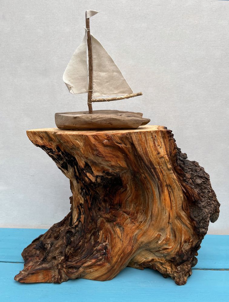 Holzstück in Form einer Welle mit Segelboot aus Treibholz darauf