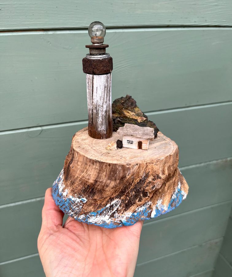Astscheibe unten in Meeresoptik bemalt, darauf eine Miniaturansicht mit Leuchtturm und Häuschen.