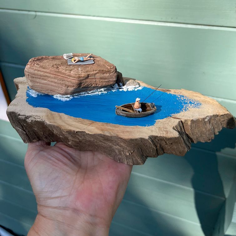 Miniaturszene mit sonnenbadender Frau auf Felsen und Angler im Boot