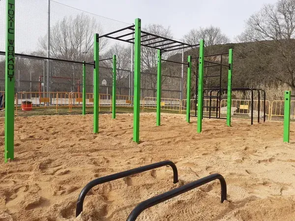 Parque de calistenia sobre arena con estructuras de street workout y barras de entrenamiento exterior