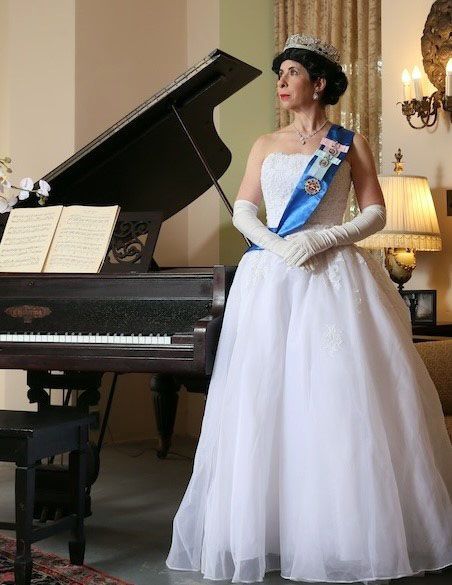 Queen Elizabeth standing next to a piano wearing a royal sash