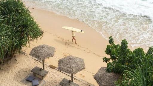 Morena Boutique Hotel Midigama Blick auf den Strand und den Inischen Ozean vor dem Morena Boutique Hotel in Midigama. Ein Surfer geht mit seinem Surfboard vorbei.