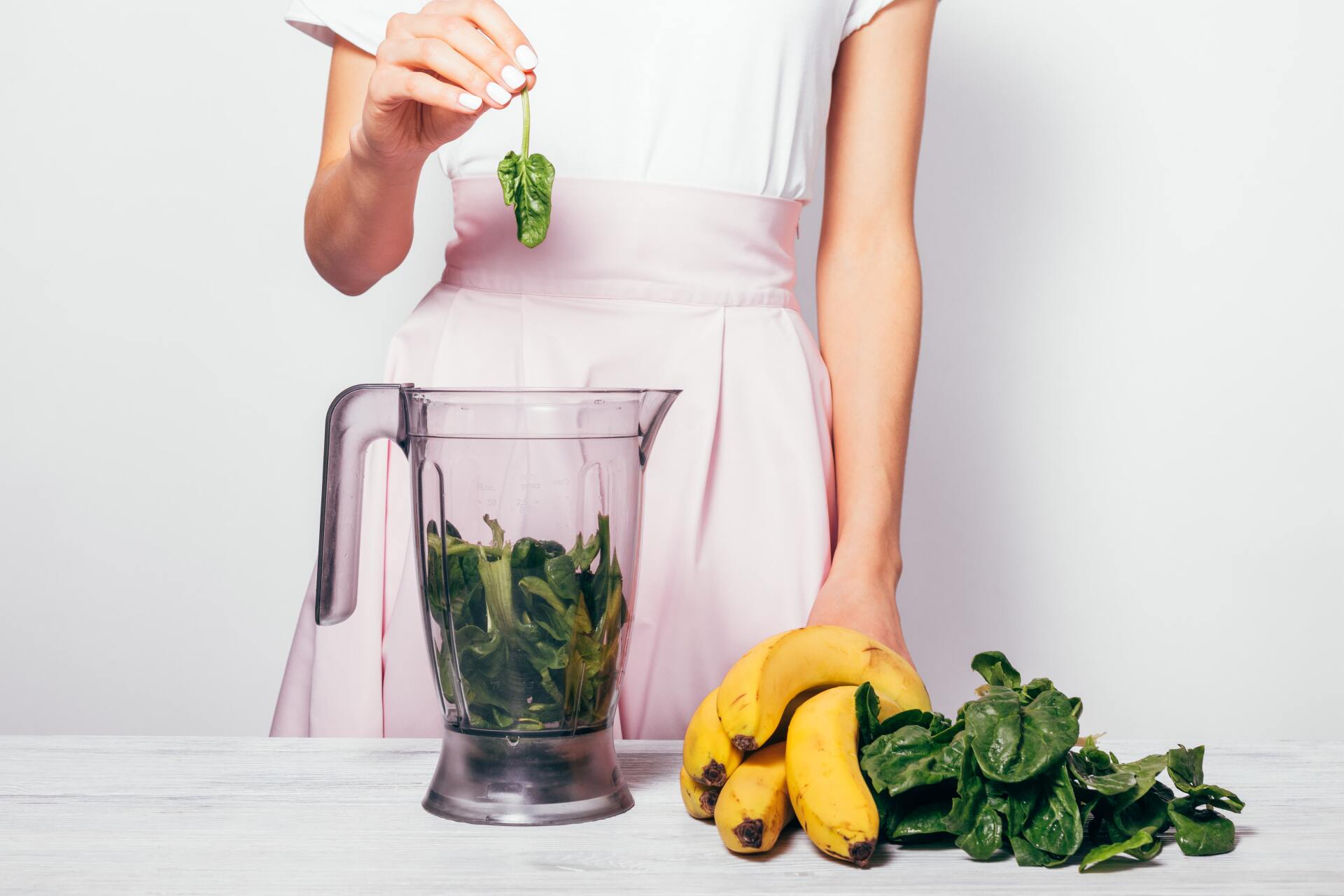 Ein Smoothie Behälter, daneben Bananen und Spinat