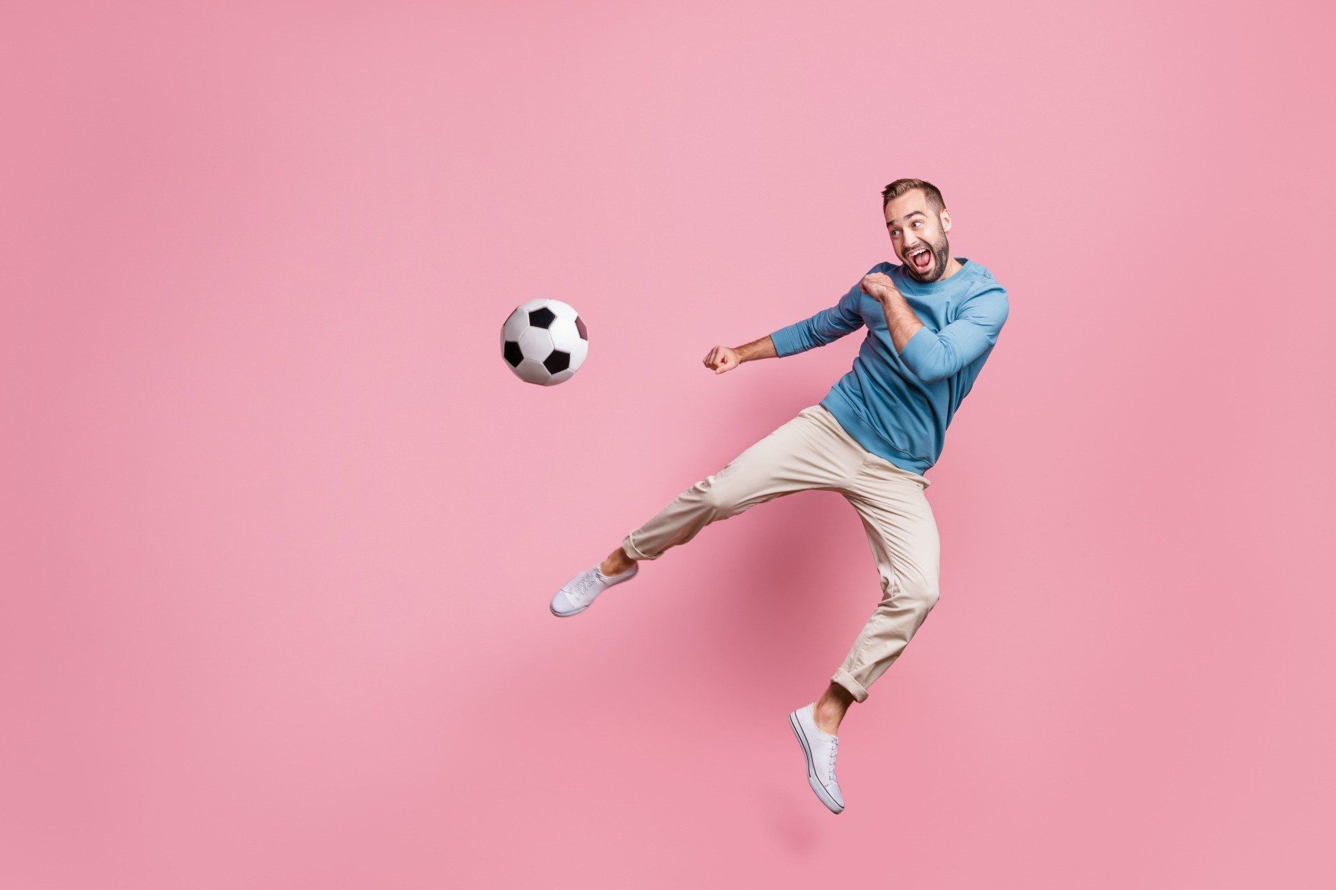 Ein fröhlicher Mann der springt und auf einen Fußball zielt
