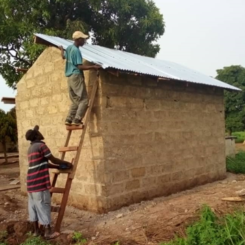 Zwei ghanaische Bauarbeiter setzten das neue Wellblechdach des Mühlhauses ein.