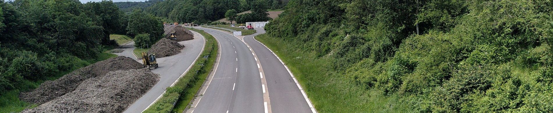 Foto der stillgelegten A 45 von oben auf die Fahrbahn. Es fahren keine Autos, rechts und links sind grüne Bäume und Büsche, links türmen sich Erdhübel auf.