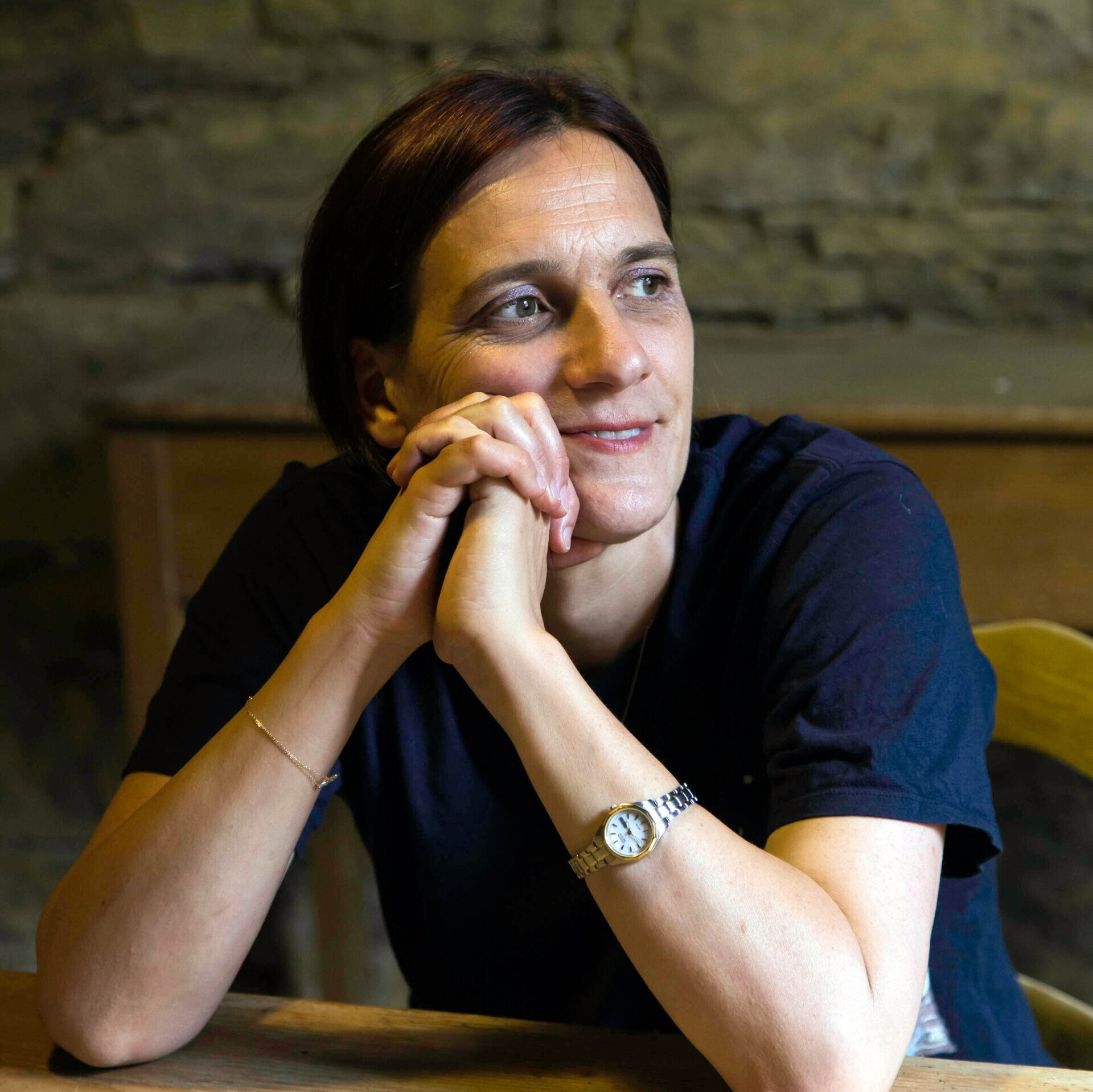 Die Autorin sitzt in der Wendener Hütte an eineme Tisch, die Ellebogen aufgestützt und das Gesichts in die gefalteten Hände seitlich abgelegt.