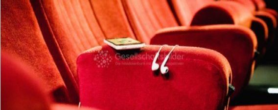 Rote Theater- oder Kinosessel, über einer Lehne liegen kleine Kopfhörer und ein Smartphone