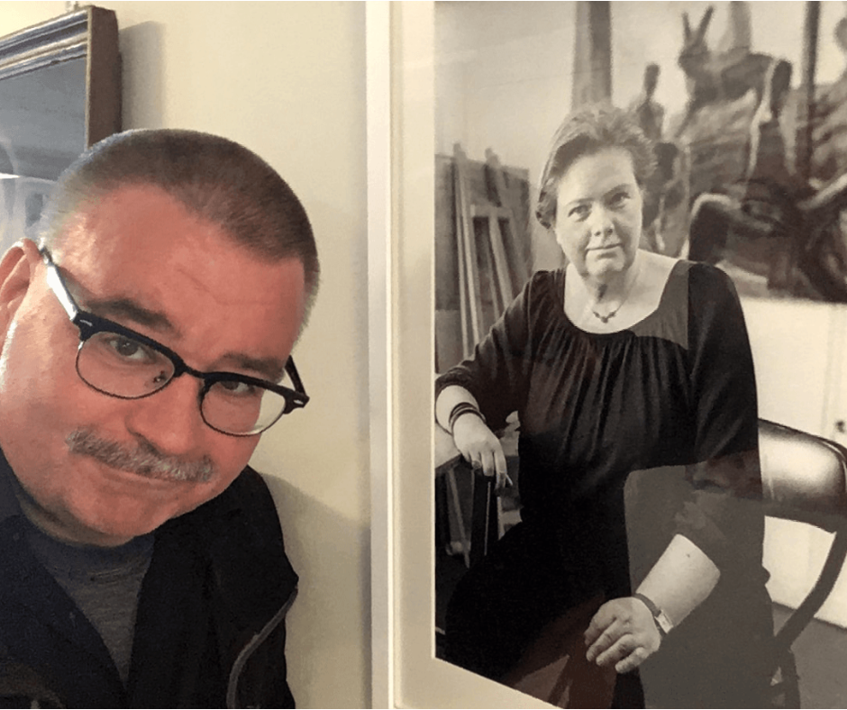 Dirk Vogel schaut seitlich in die Kamera, rechts neben ihm hängt ein schwarz-weiß Foto einer Künstlerin, das er fotografiert hat.