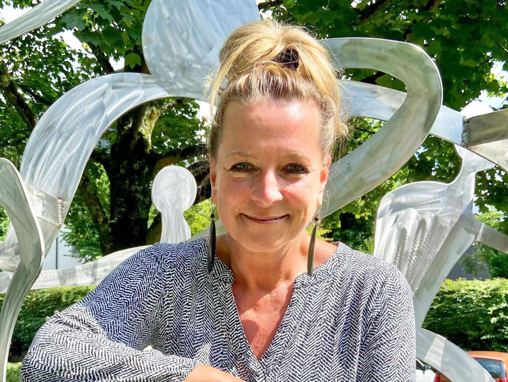 Frau Dr. Tretow steht lächelnd in einem Park, im Hintergrund ist eine metallisch glänzende Skulptur zu sehen