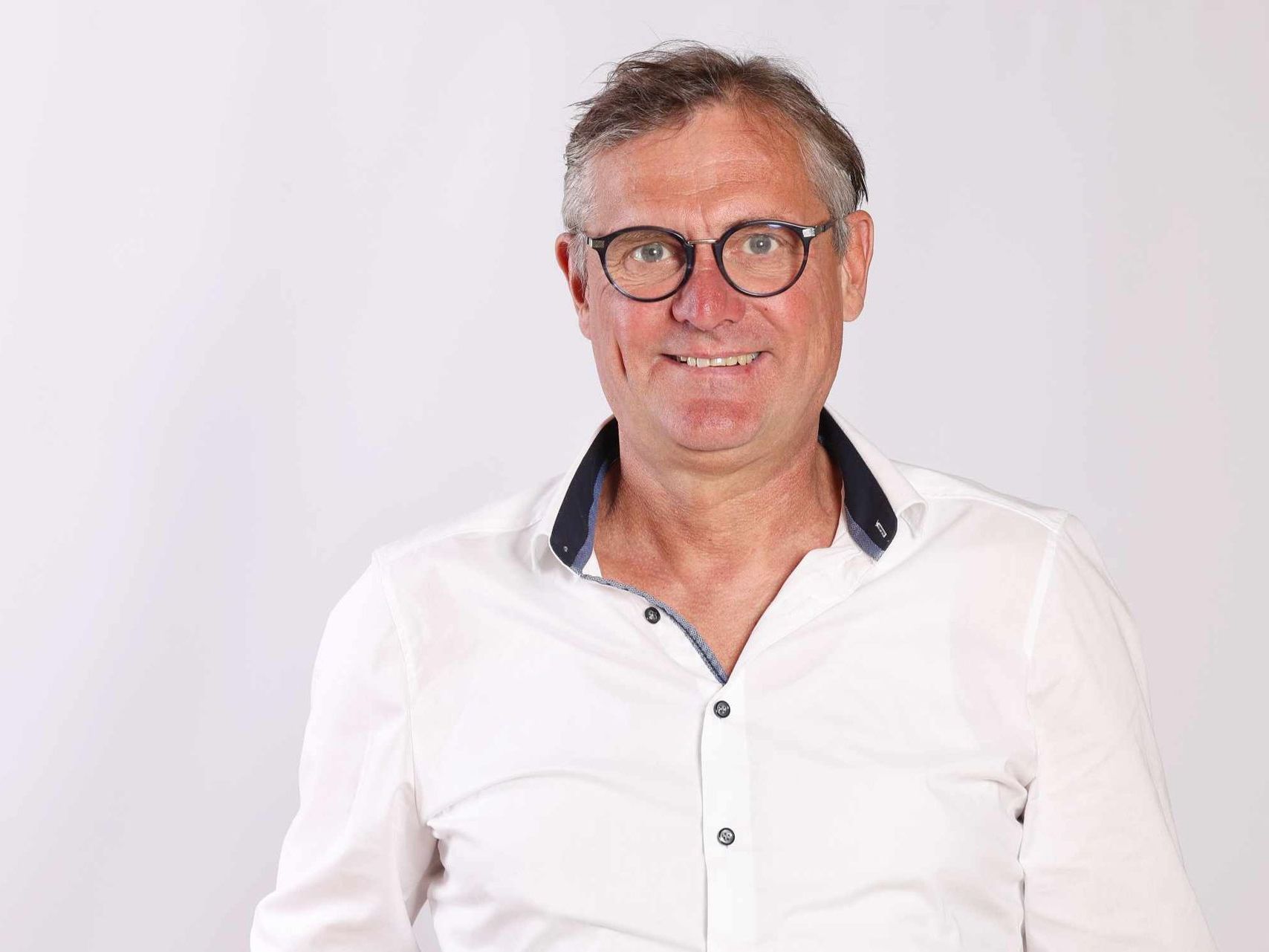 Frank Büdenbender in weißem Hemd vor hellem Hintergrund lächelt in die Kamera