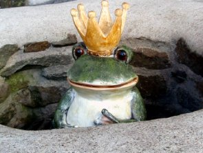 Froschkönig aus Steingut mit Krone schaut aus einem Brunen