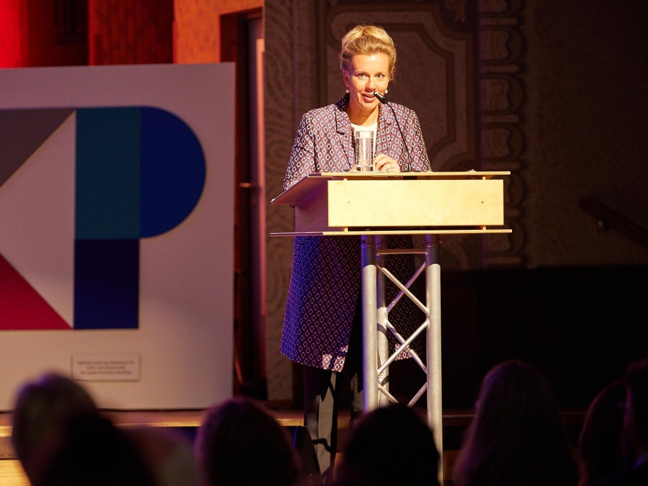 Kulturministerin Ina Brandes steht auf der Bühne vor einem Podium und spricht zu den Zuschauern.