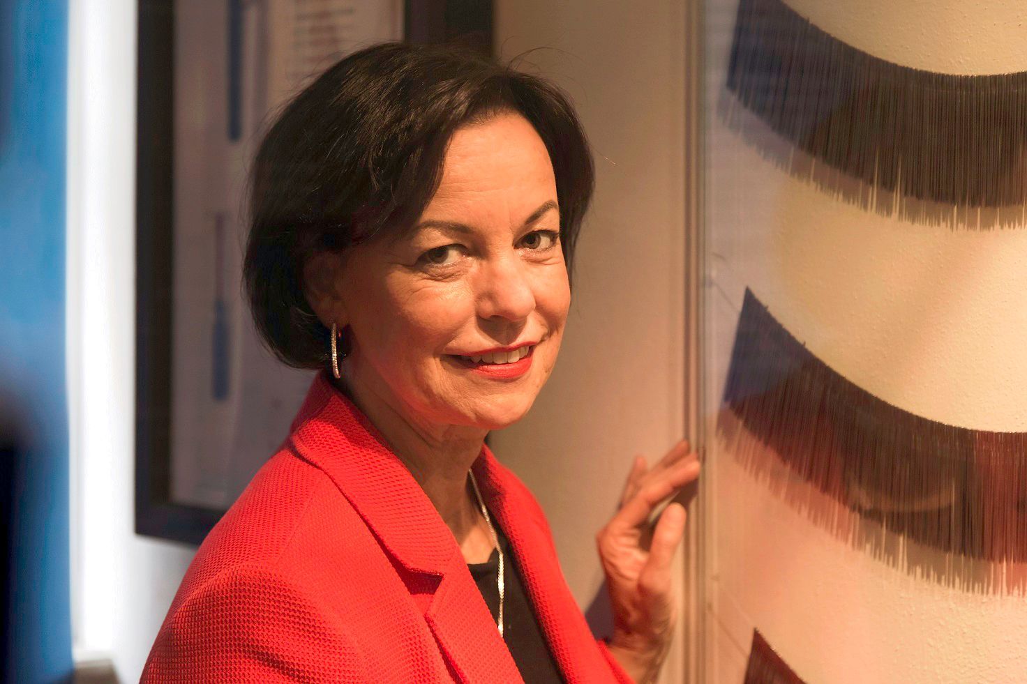 Jutta Törnig-Struck steht im Museum vor einem flachen Glasrahmen an der Wand, hinter dem alte Nadeln zu sehen sind. Die Nadeln sind wie Colliers aufgereiht.