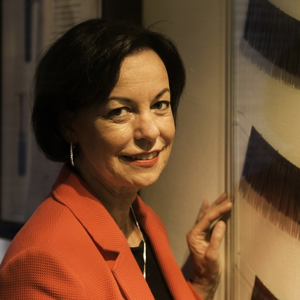 Jutta Törnig-Struck steht im Museum vor einem flachen Glasrahmen an der Wand, hinter dem alte Nadeln zu sehen sind. Die Nadeln sind wie Colliers aufgereiht.