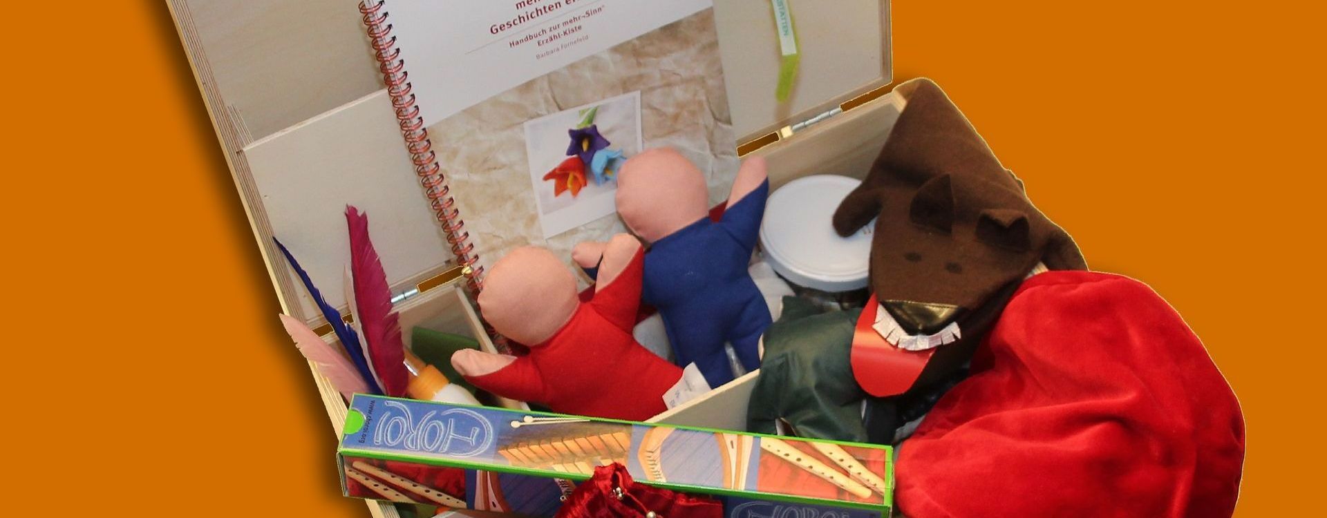Geöffneter Mehrsinn-Erzählkoffer mit Requisiten wie Handpuppen, Stoffe, Büch, Kissen u.a.