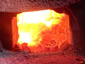 Geöffneter Schmiedeofen, in dem die glühende Kohle zu sehen ist.