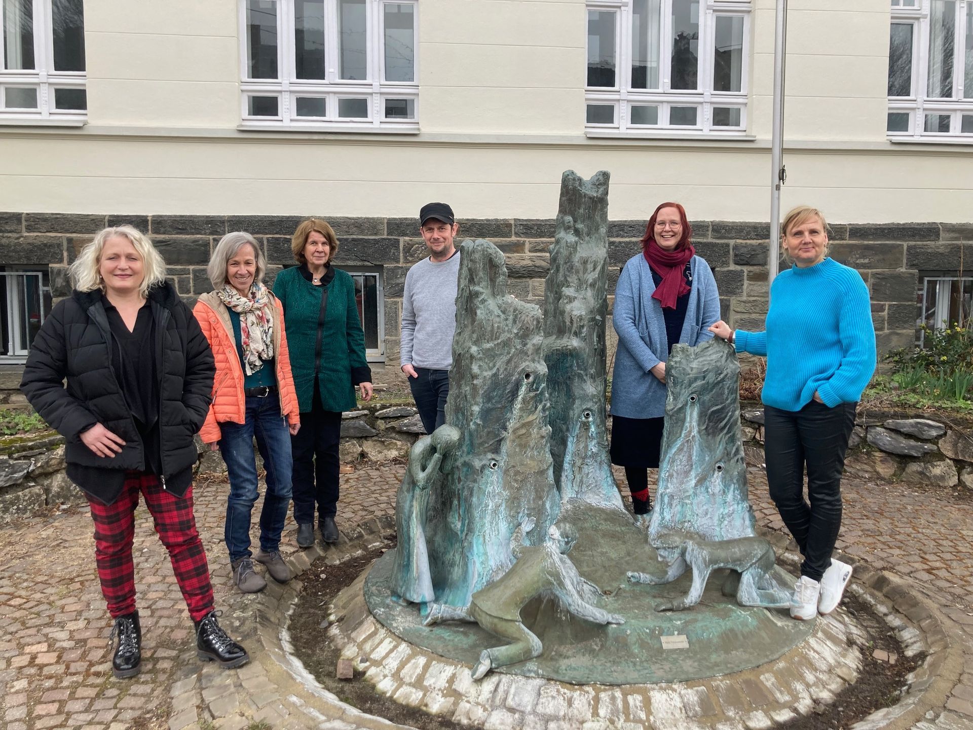 Die sechs Akteur:innen des Kulturstammtisches stehen draußen um eine Figurengruppe aus Stein.