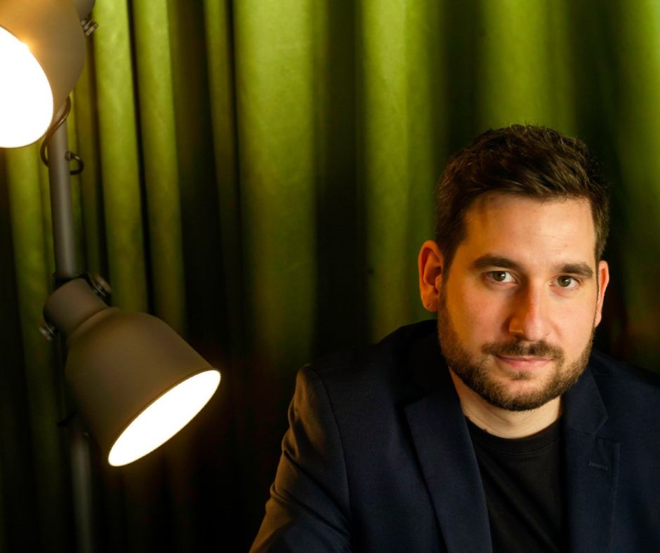 Großaufnahme das Gesichts von Marc Debie vor einem grünen blickdichten Vorgang. Links neben ihn stehe eine Lampe mit zwei Leuchten, die Lichtimpulse setzen.