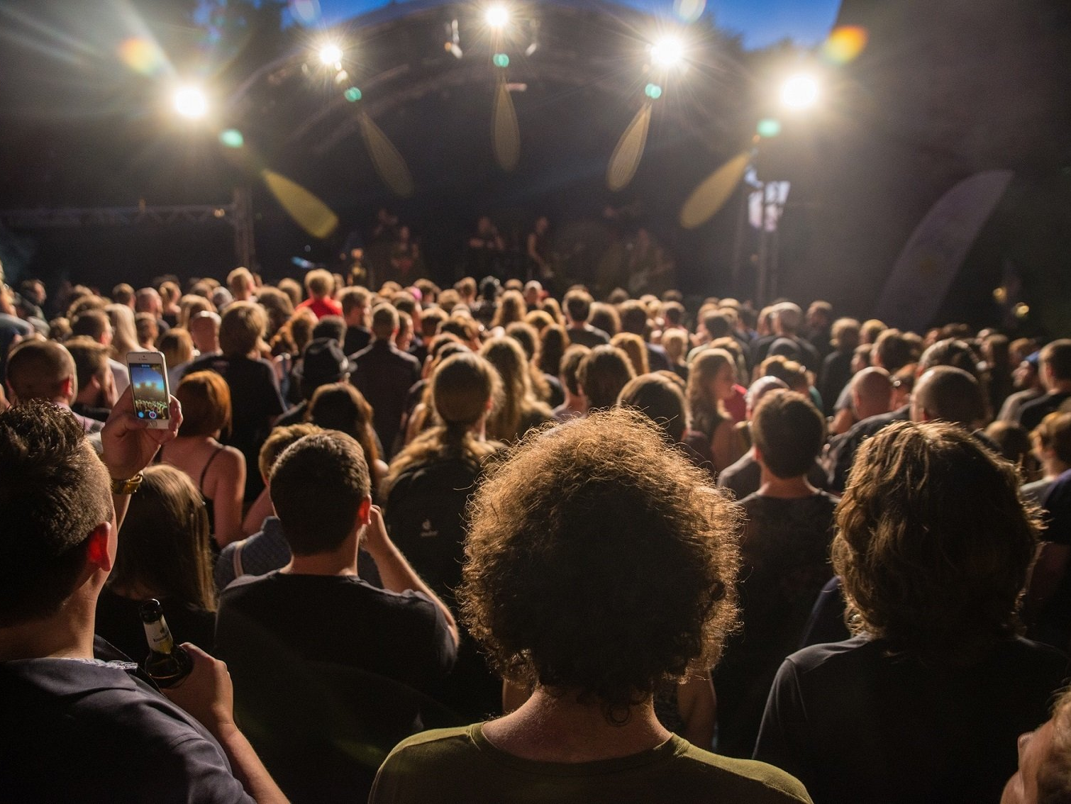 Menschenmenge vor einer Bühne, von hinten fotografiert. Auf der Bühne spielt eine Band.