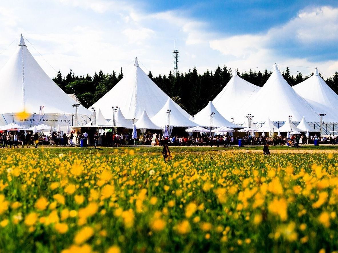 Foto des Festivals Kulturpur mit seinen großen weißen Zelten auf einer Wiese, die mit gelben Blumen übersät ist.