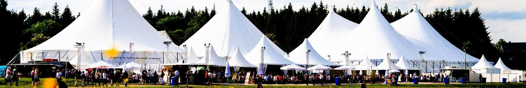 Zeltfestival KulturPur auf dem Giller bei schönstem Wetter, gelber Löwenzahn im Vordergrund, im Hintergrund sind die weißen Zelte mit einer Menschenmenge zu sehen.