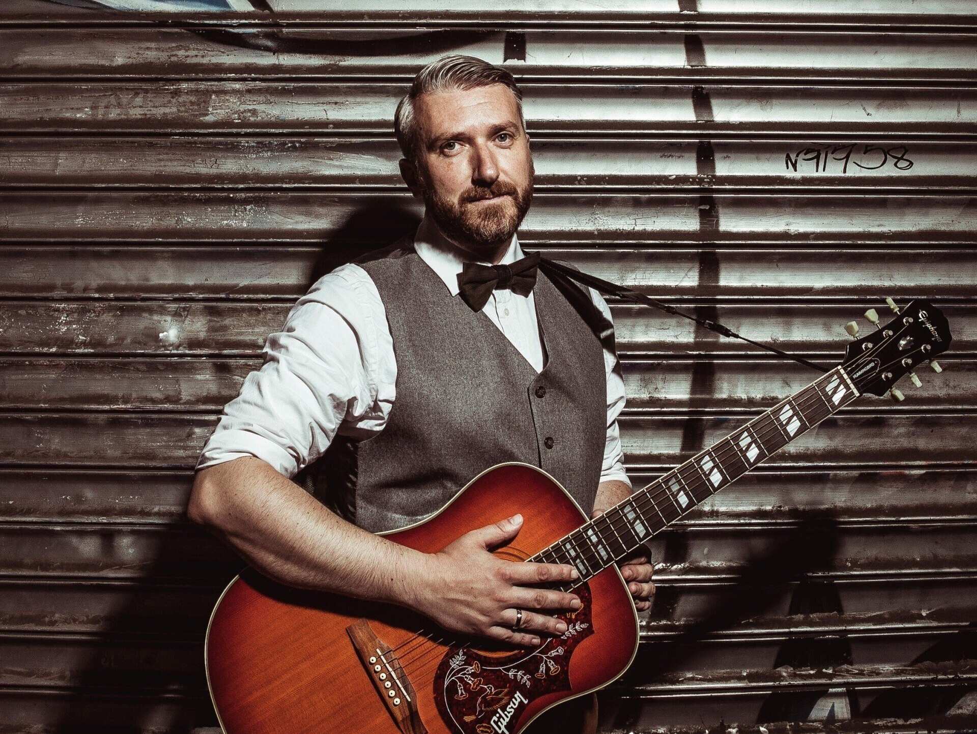 Sebastian Wagemeyer steht vor einem Wellblechtor, eine Gitarre umgehängt.