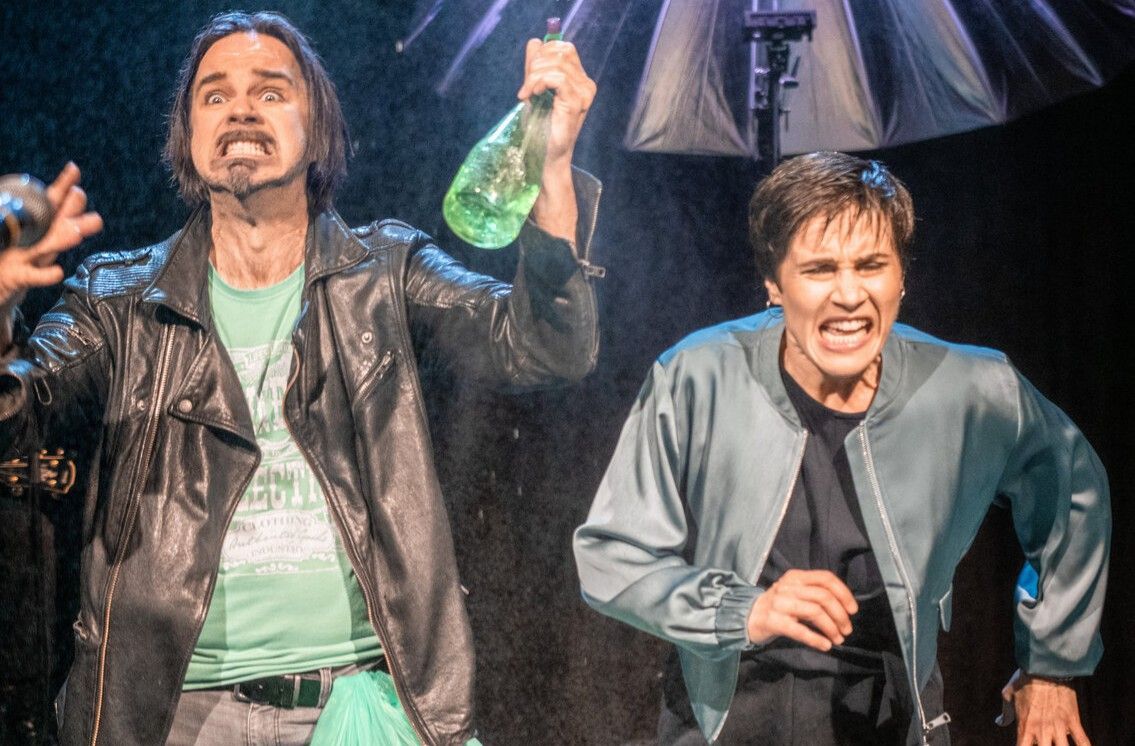 Foto der Bühnensituation: ein Schauspieler und eine Schauspielerin rennen durch Regen.