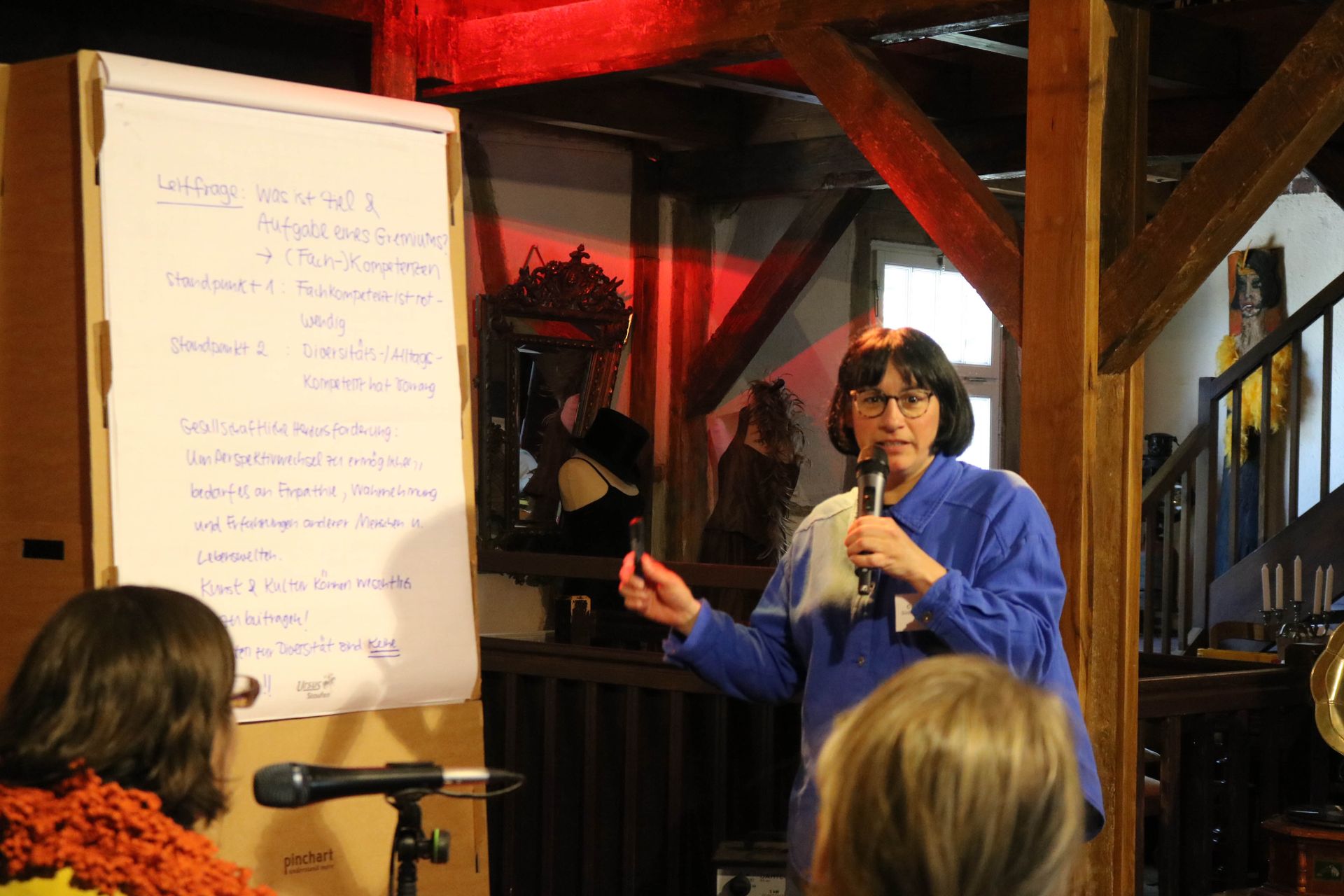 Frau Krell steht auf der Bühne vor dem Flipchart und präsentiert ein Workshopergebnis.