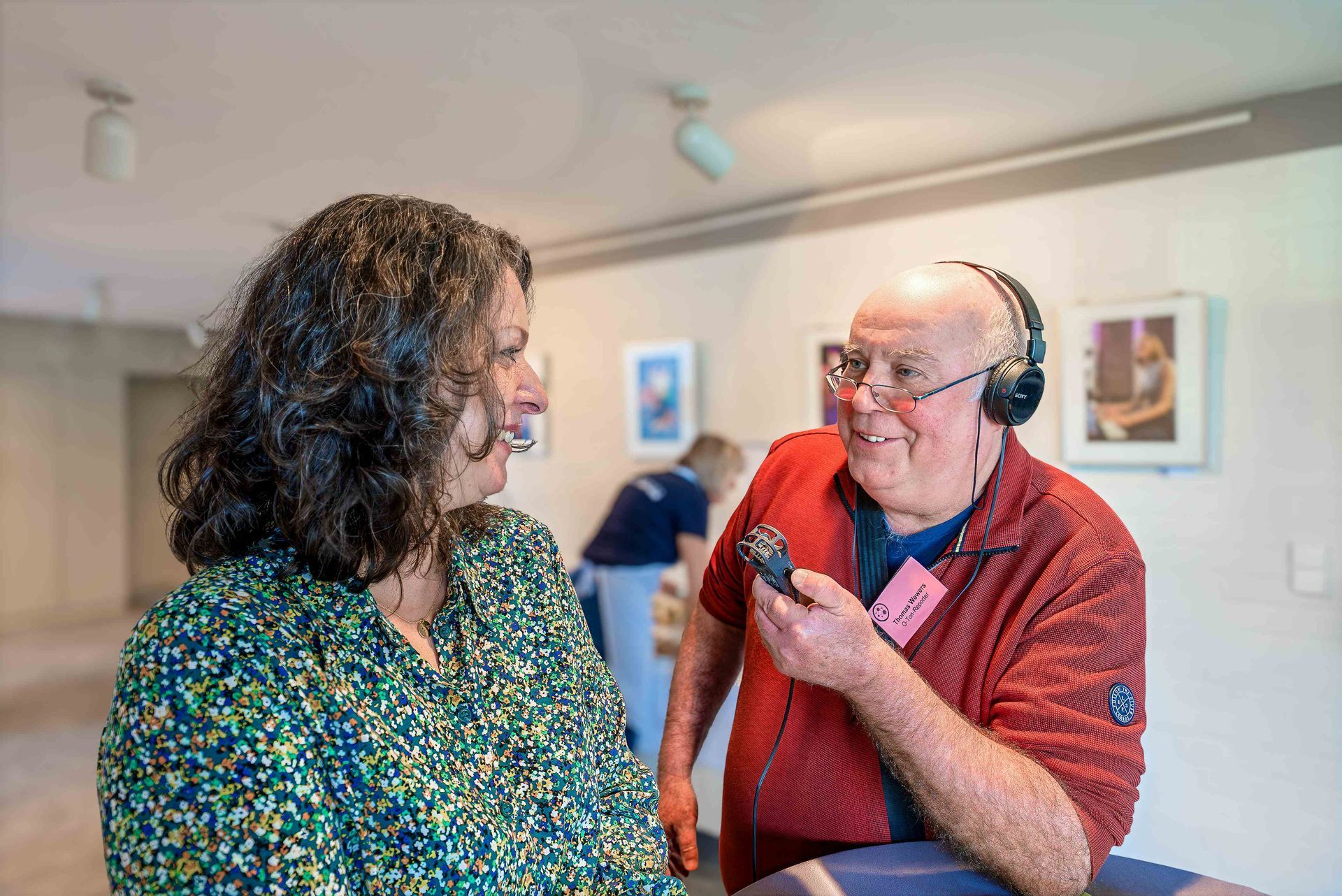Thomas Wewers trägt Kopfhörer und hält ein Mikrofon in der Hand, der er Silke Scharpe hinhält. Er schaut Silke Scharpe an, sie lächelt zurück.