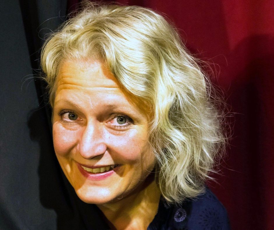 Porträtaufnahme von Ulrike Wesely, die zwischen einem schwarz-roten Theatervorhand hervorschaut und in die Kamera lächelt.