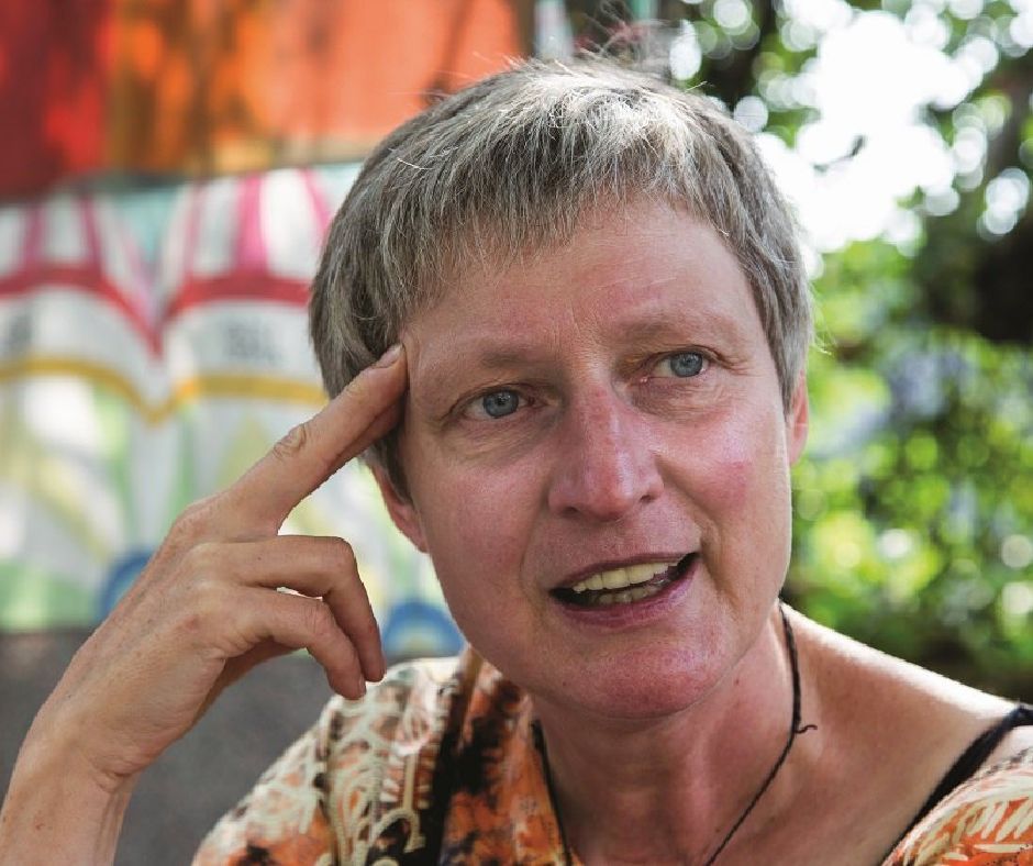 Porträtaufnahme der Erzählerin, die in nachdenkler Pose im  Garten sitzt, den Kopf mit der rechten Schläfe auf die Fingerspitzen einer Hand abgestützt.