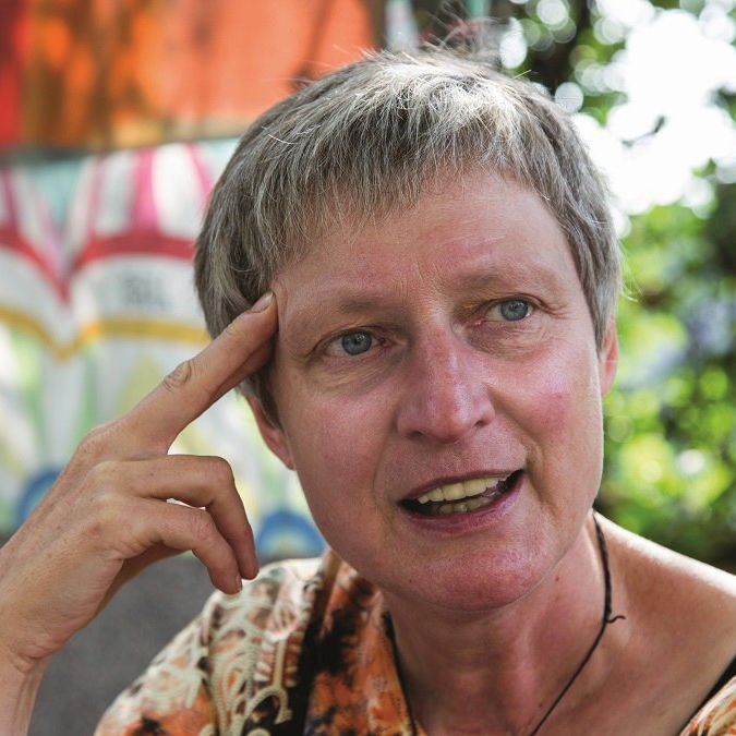 Porträtaufnahme der Erzählerin, die in nachdenkler Pose im Garten sitzt, den Kopf mit der rechten Schläfe auf die Fingerspitzen einer Hand abgestützt.